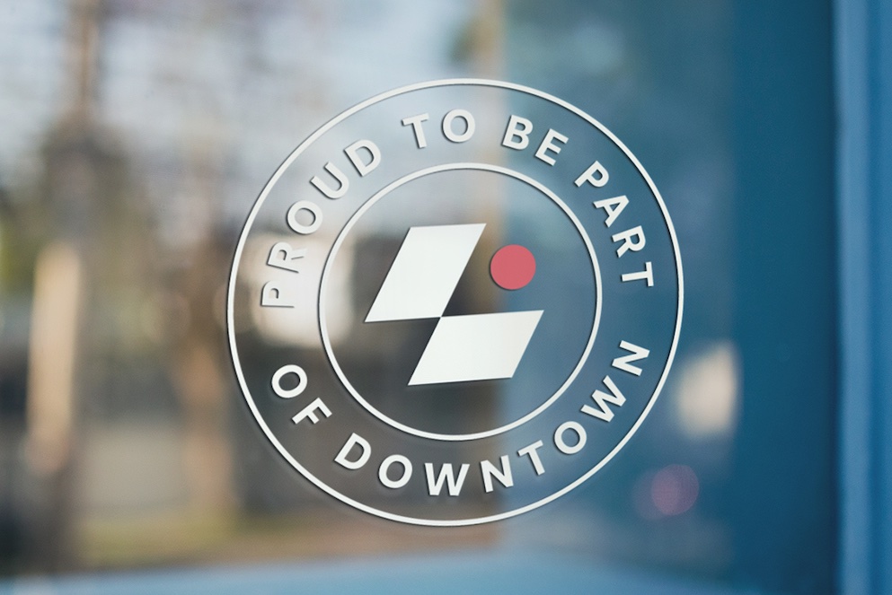 A window cling displays the geometric logo for Downtown Lansing Inc. and reads "Proud to be part of downtown"