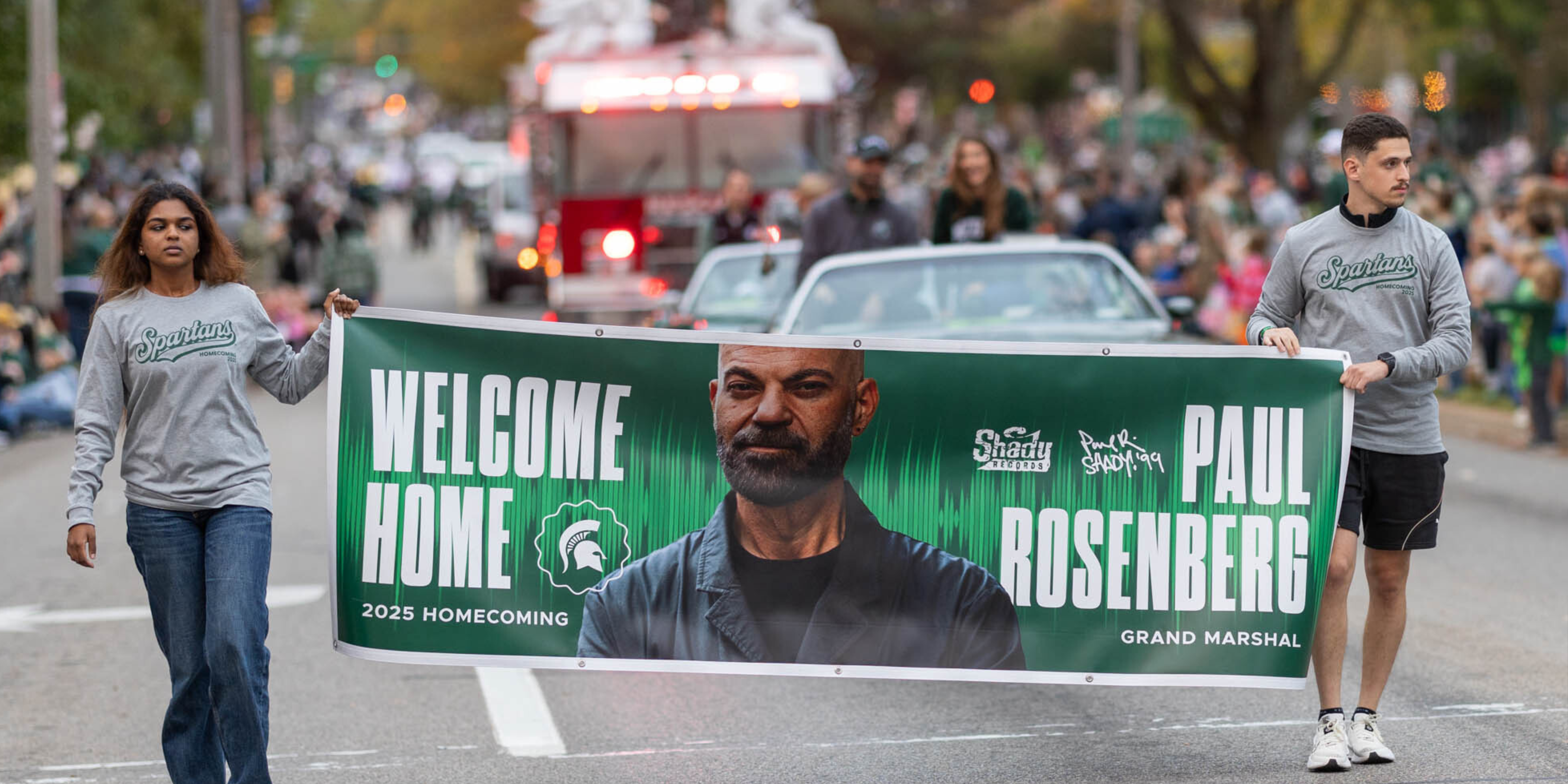 A banner for the MSU Homecoming parade shows a picture of Paul Rosenberg's face with the text "Welcome Home Paul Rosenberg"