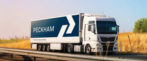 A semi-truck displays the Peckham logo, in white font in front of a blue background. 