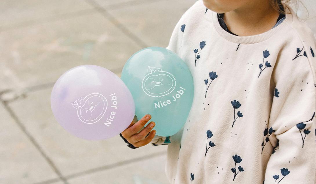 Child holding balloons with cartoon sloth design on them.