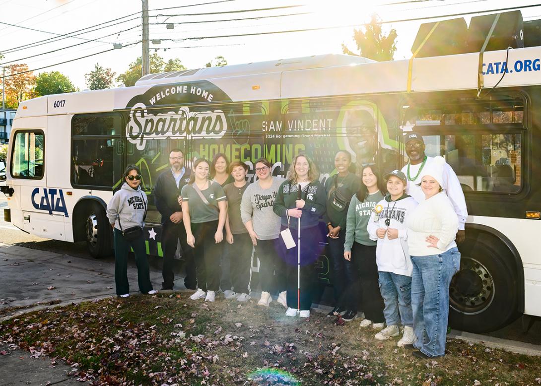 Crowd of people wearing MSU homecoming gear standing in front of bus with MSU Homecoming branded wrap design.